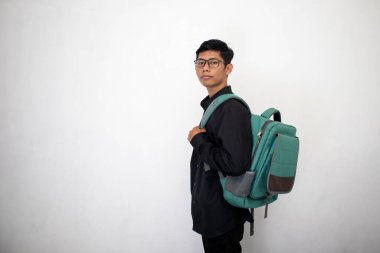 Temiz siyah elbiseli Asyalı bir adam beyaz arka planda yeşil bir sırt çantası taşıyor. Kendine güveni olan bir öğrenci..