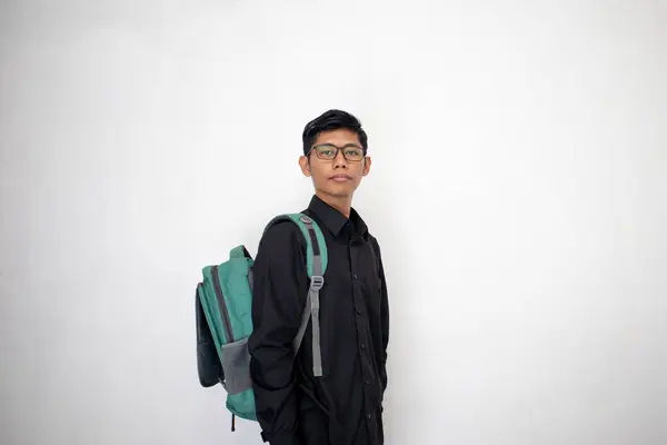 Asian man in neat black clothes is carrying a green backpack on a white background. a student carrying a bag with confidence.