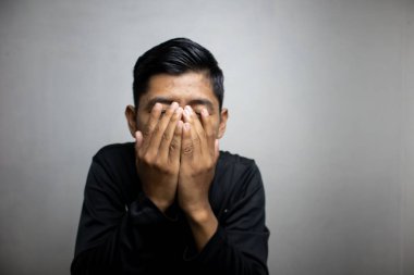 Siyah elbiseli duygusal Asyalı adam beyaz stüdyo arka planında poz veriyor. 