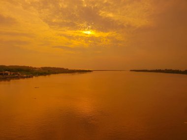 Gün batımında bulutlu gökyüzünün altındaki sakin nehrin manzarası, Endonezya 