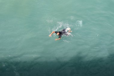 Genç adam okyanusta yüzüyor, iskeleye yakın.