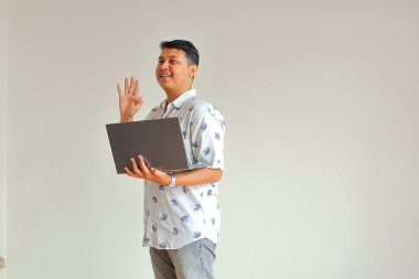 Asyalı iş adamı dizüstü bilgisayarını tutuyor ve el sallıyor. 