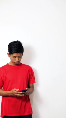 Asyalı genç yakışıklı Asyalı sıradan tişörtler giyiyor. Beyaz arka planda izole edilmiş video görüşmesi için akıllı telefon kullanıyor.