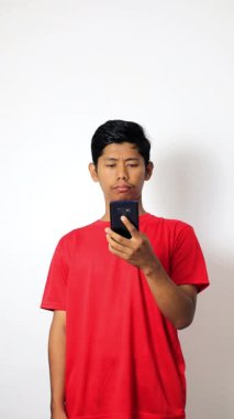 Beyaz arka planda izole edilmiş akıllı telefonunu kullanan kırmızı tişörtlü bir Asyalı.