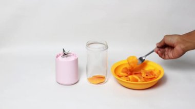 Mango suyu yapımında kullanılan küçük taşınabilir blender, beyaz arka planda taze mango suyu.