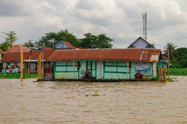 Palembang, 22 Aralık 2024: Durgun bir köyde bulutlu bir gökyüzünün altında yüzen evler ve nehir hayatı