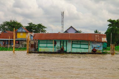 Palembang, 22 Aralık 2024: Durgun bir köyde bulutlu bir gökyüzünün altında yüzen evler ve nehir hayatı