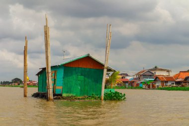Palembang, 22 Aralık 2024: Durgun bir köyde bulutlu bir gökyüzünün altında yüzen evler ve nehir hayatı