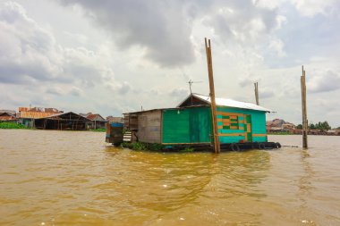 Palembang, 22 Aralık 2024: Durgun bir köyde bulutlu bir gökyüzünün altında yüzen evler ve nehir hayatı