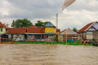 Palembang, 22 Aralık 2024: Bulutlu gökyüzü altında eşsiz bir mimari ve yemyeşil bitki örtüsüne sahip nehir kenarı köyü.