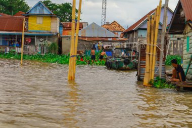 Palembang, 22 Aralık 2024: Bulutlu gökyüzü altında eşsiz bir mimari ve yemyeşil bitki örtüsüne sahip nehir kenarı köyü.
