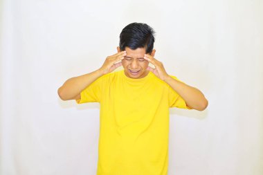 Sarı tişörtlü, başı ağrıyan genç yakışıklı Asyalı adam izole edilmiş arka planda duruyor. 