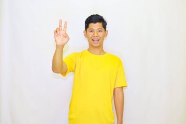 Sarı tişört giyen genç Asyalı adam iki parmağını izole edilmiş beyaz arka plan gösteriyor. 