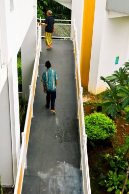 Bakauheni, 17 Ocak 2025, yakınındaki beyaz korkuluklar ve bitkilerle yükseltilmiş bir yürüyüş yolu boyunca iki kişi yürür..