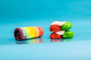 Yığınla renkli şekerin yanında canlı bir gökkuşağı pastası. Tatlı ikramlar, pürüzsüz bir arka planda.