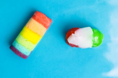 Canlı bir gökkuşağı pastası ve parlak mavi bir arka planda renkli jöle şekeri. Tatlı ikram konsepti.