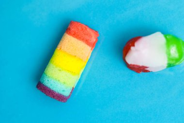 Canlı bir gökkuşağı pastası ve parlak mavi bir arka planda renkli şekerler..