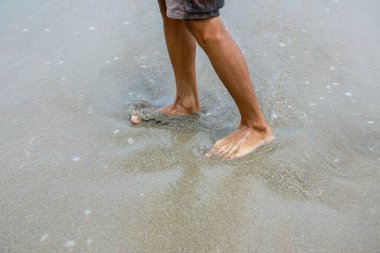 Kumsalda çıplak ayakla yürüyen bir adamın, huzurlu okyanus dalgalarının tadını çıkarırken..