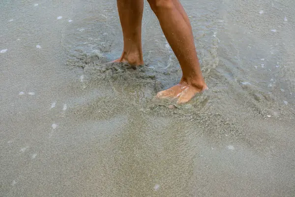 Çıplak ayaklar okyanus suyunda süzülüyor, deniz kenarında tatilin tadını çıkarıyor..