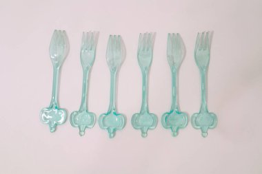 Beyaz arka planda altı sıra açık mavi plastik çatal bulunur.