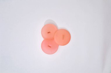 Açık beyaz tekstil yüzeyinde duran üç soluk pembe düğme.