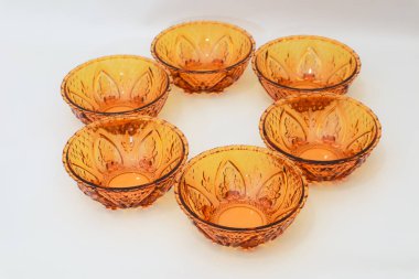 Kehribar rengi altı cam kaseden oluşan dairesel bir düzenleme. Temiz, minimalist beyaz bir zemin üzerinde.