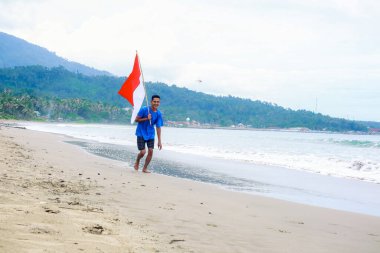 Genç bir adam güzel bir sahilde Bağımsızlık Günü 'nü bayrağıyla kutluyor.