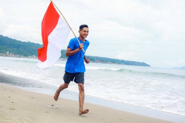 Adam sevinçle koşar sahilde Endonezya bayrağını sallayarak bağımsızlık gününü kutlar