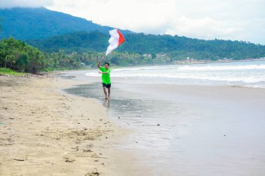 Endonezya 'nın Bağımsızlık Günü' nü kutlayan genç adam sahilde kırmızı ve beyaz bayrak sallıyor.