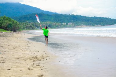 Genç adam coşkuyla bayrak sallıyor tropikal sahilde Bağımsızlık Günü 'nü kutluyor