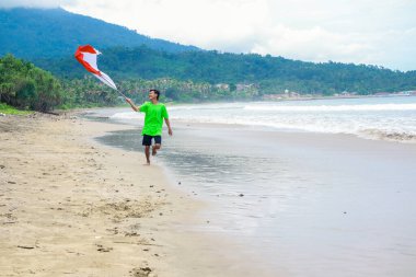 Endonezya 'nın Bağımsızlık Günü' nü kutlayan genç adam güzel bir sahilde kırmızı ve beyaz bayrak sallayarak koşuyor.