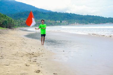 Endonezya Bağımsızlık Günü 'nü güzel bir plajda neşeyle kutlayan genç bir adam..