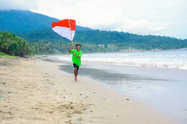 Genç Endonezyalı bir adam Bağımsızlık Günü kutlamalarında sahilde sevinçle koşar.