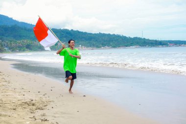 Endonezya Bağımsızlık Günü 'nü plajda bayrağıyla kutlayan coşkulu bir adam.