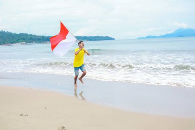 Endonezya bayrağıyla sahilde koşan bir adam Bağımsızlık Günü 'nü kutluyor.