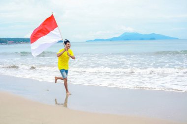 Adam sahilde neşeyle koşuyor, Endonezya bayrağını sallıyor, Bağımsızlık Günü 'nü kutluyor.