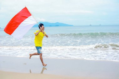 Genç adam bağımsızlık gününü sahilde bayrak sallayarak kutluyor.