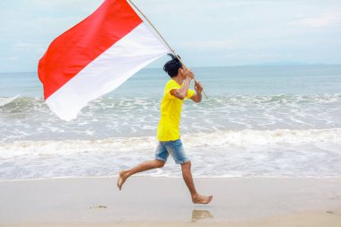 Genç bir adam ulusal bayrağı elinde tutarak sahilde yalınayak koşan özgürlüğünü kutluyor.
