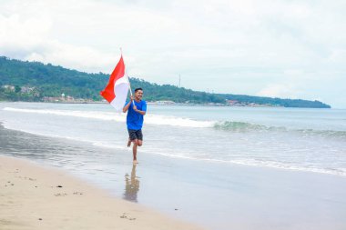 Bağımsızlık gününde sahilde koşan Endonezya bayrağıyla hevesli bir adam.