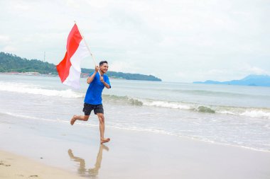 Gülümseyen bir adam güzel bir sahil manzarasında Endonezya bayrağıyla neşeyle koşar.