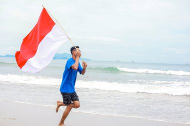 Genç adam sevinçle sahilde koşuyor, Bağımsızlık Günü 'nü bayrağıyla kutluyor.