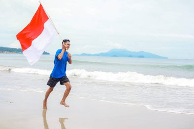 Genç adam sahilde Bağımsızlık Günü 'nü kutlayan Endonezya bayrağını neşeyle taşıyor.