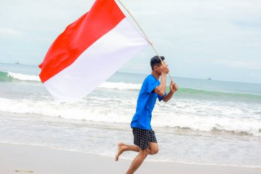 Endonezya bayrağını taşıyan genç bir adam sahilde coşkuyla koşuyor.