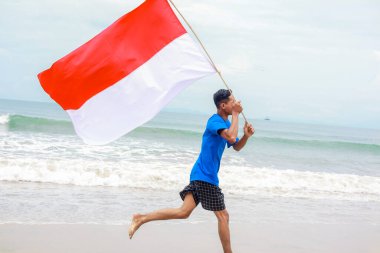 Genç bir adam sevinçle sahilde koşuyor, Endonezya bayrağını sallıyor, Bağımsızlık Günü 'nü kutluyor.