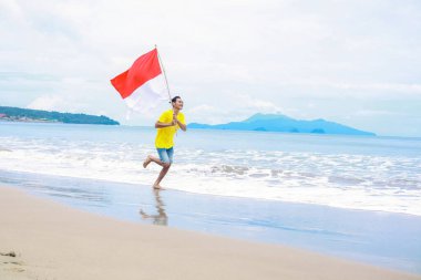 Bağımsızlık Günü 'nü kutlayan Endonezya bayrağıyla sahilde koşan bir adam.