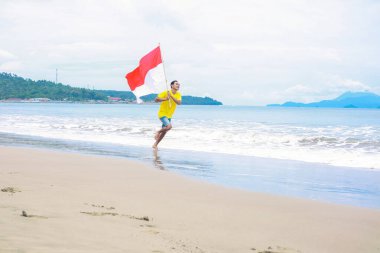 Endonezya 'nın Bağımsızlık Günü' nü kutlayan bir adam plajda bayrağıyla koşuyor.