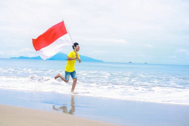 Genç bir adam, Endonezya 'nın Bağımsızlık Günü' nü sahilde bayrak sallayarak kutluyor.