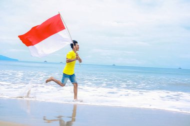 Genç adam Endonezya 'nın Bağımsızlık Günü' nü güzel bir plajda ulusal bayrağıyla kutluyor.