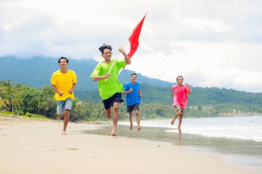 Dört genç adam sahilde bayrağıyla koşuyor özgürlüğün ve kutlamanın tadını çıkarıyor.