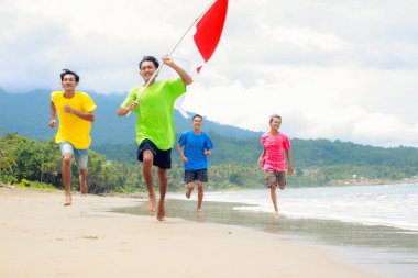 Sahilde koşuşturan bir grup neşeli genç Endonezya Bağımsızlık Günü 'nü kutluyor.
